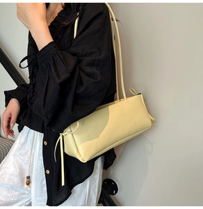 Detailopname van de crème baguette-tas met decoratieve trekkoorden aan de zijkant