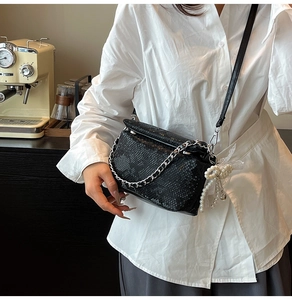 Detail van zwarte crossbodytas met krokodillentextuur, zilveren ketting en parelhanger