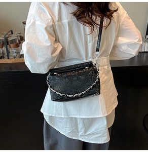 Modelaanzicht van zwarte crossbodytas met slangenpatroon en zilveren ketting