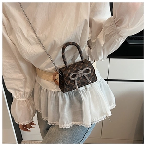 Brown mini handbag with rhinestone bow and chain strap shown on model's shoulder