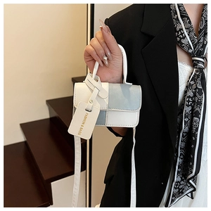 Close-up of stylish two-tone mini handbag with elegant gold-lettered leather hangtag