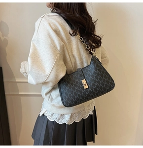 Model wearing a black monogram handbag with gold chain strap and metallic buckle