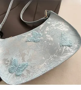 Dettaglio della borsa a mezzaluna azzurra con motivi in pizzo e farfalle applicate in 3D