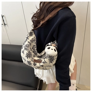 Detailed side view of canvas crescent bag with embroidery and panda plush charm