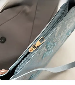 Dettaglio della cerniera dorata e del ricamo sulla borsa a spalla in pizzo blu da donna