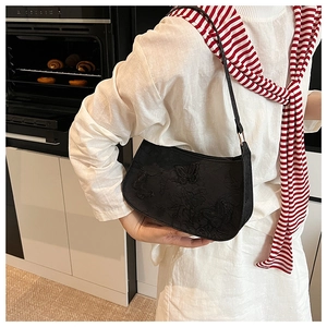 Détail d'un sac sous le bras noir avec broderie papillon 3D et boucles métalliques dorées