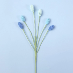 Detail of six blue handmade crochet flower buds with gradient yarn textures and green stems