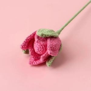 Detailed close-up of handmade crochet pink rose with green leaves and soft yarn texture