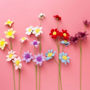 Detail of colorful handmade crochet daisy flowers with green stems on a pink background