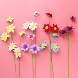 Close-up of colorful handmade crochet daisies and cosmos flowers on a pink background