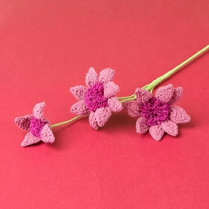 Detail of three handmade crochet daisies with pink petals and green stems on red background