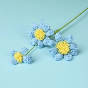 Detail of handcrafted crochet blue daisies with soft yellow centers and green stems