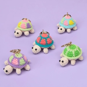 Set of five handmade crochet turtle keychains with colorful shells on a purple background