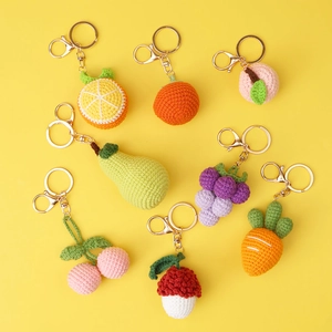 Handmade crochet fruit keychain set featuring grapes peach and orange on yellow background