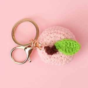 Detail of a handmade crochet peach keychain with pink yarn and golden metal ring