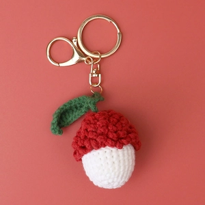Macro detail of a handmade crochet lychee keychain with gold metal clasp on coral background