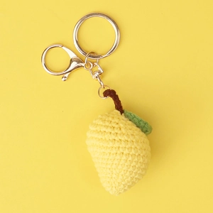 Macro shot of handmade crochet lemon pendant with green leaf and golden metal keychain