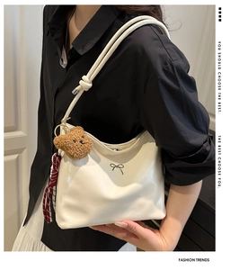 Detail der weißen glänzenden Ledertasche mit silberner Schleife und Bärenanhänger