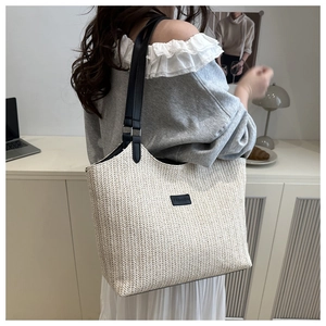 Detailed view of woven straw tote bag texture with fashion label and leather straps