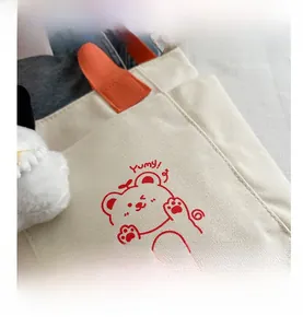 Close-up of off-white canvas tote with orange handle and red cartoon bear design