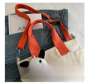 Detail of white canvas tote with orange strap, red cartoon bear print and plush charm