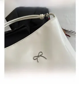 Close-up of white PU leather bucket bag with silver metal bow and knotted strap detail