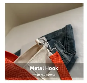 Detail of silver metal lobster hook on canvas tote bag with orange woven shoulder strap