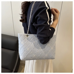 Detail view of light blue embroidered tote bag with gold chain strap on shoulder