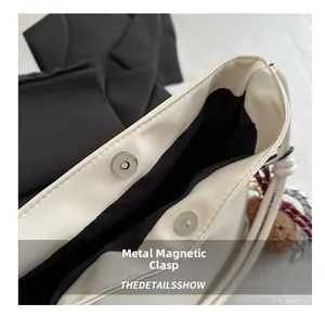 Detailed macro view of the metal magnetic buckle on the white leather tote bag
