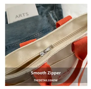 Detailed close-up of smooth silver zipper closure on stylish canvas tote bag with orange straps