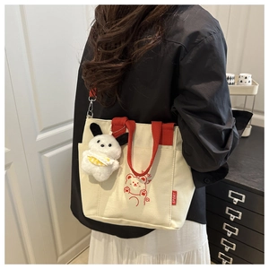 Detail of canvas tote bag featuring cute red bear print and plush puppy pendant accessory