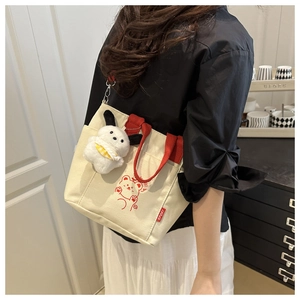 Detail of canvas tote bag with red handles, cartoon bear print and plush dog pendant
