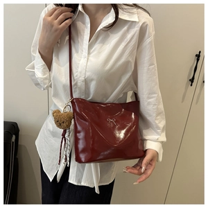 Detail of dark red glossy leather bucket bag with silver bow and plush bear charm
