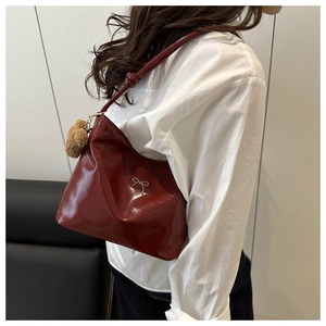 Detail of glossy wine red shoulder bag with silver bow and plush bear charm accent