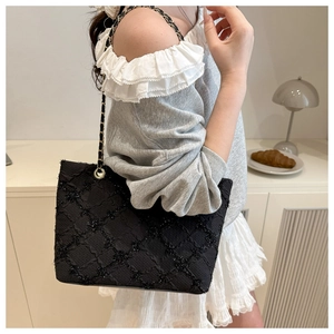Detail of black quilted tote bag featuring metallic chain strap and textured diamond pattern