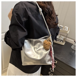 Detail of silver metallic underarm bag featuring a metal bow and brown bear charm