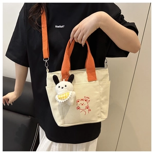 Detail of canvas tote bag showing orange straps, cartoon bear print, and plush bunny charm