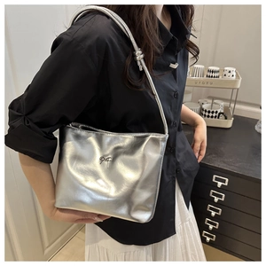 Detail of a metallic silver shoulder bag featuring a decorative metal bow and pleated leather