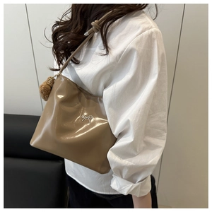 Close-up of khaki glossy shoulder bag featuring silver bow and cute plush bear charm