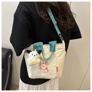 Detail of canvas tote bag with blue handles, red bear print, and plush dog charm