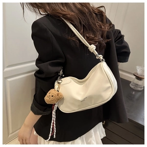 Detail van de crème hobo-tas met teddybeerhanger en geweven lint over de schouder