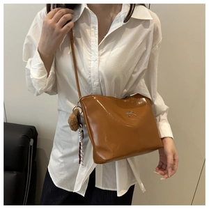 Brown leather crossbody bag with silver bow badge and plush pom-pom charm on model