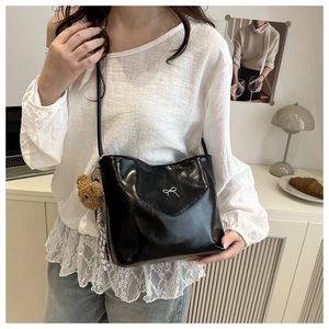Detail of black glossy leather tote bag featuring a silver bow and plush bear charm