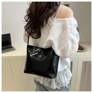 Close-up of a black glossy shoulder bag with a silver metallic bow detail