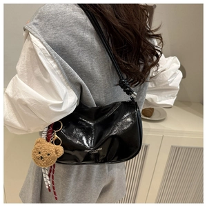 Detail of glossy black leather shoulder bag with a plush bear charm and text detail