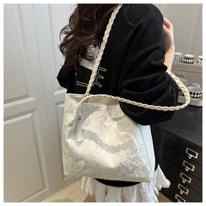 Detail of white lace tote bag with floral patterns, braided strap, and tassel charm