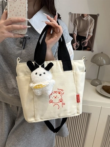 Minimalist canvas handbag with red bear print and plush toy charm in a lifestyle setting