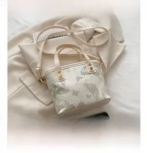 Dettaglio ricamo farfalla su borsa a secchiello crema con finiture in oro lucido