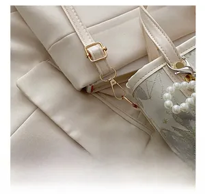 Dettaglio accessori dorati e manico di perle su borsa a secchiello ricamata bianco crema