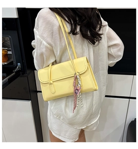 Detail of bright yellow leather tote bag with decorative charms on a woman's shoulder